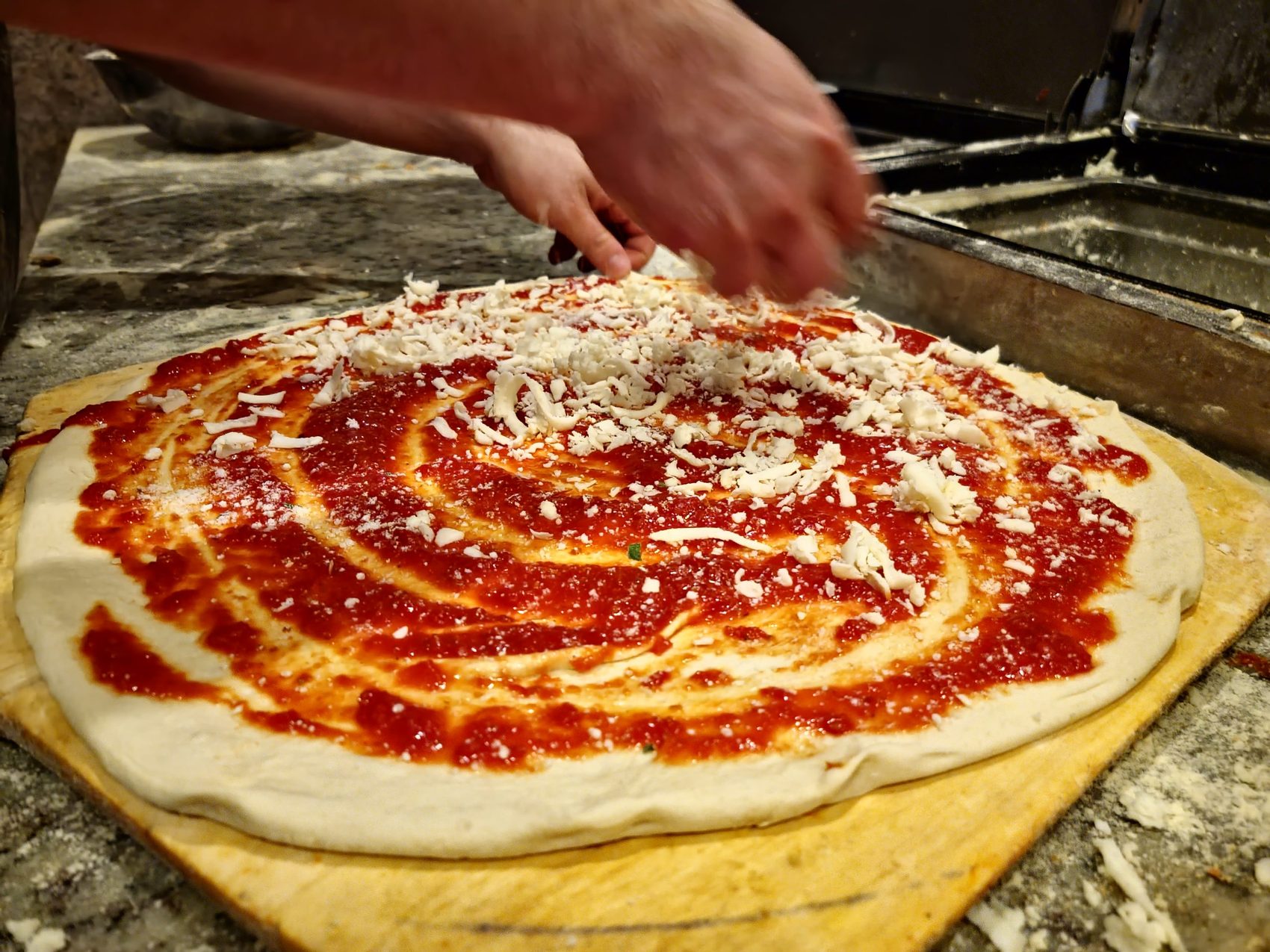 A pizza being sauced and cheesed by hand at the oven
